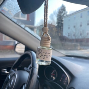 Pu&ograve; includere: Un profumatore per auto appeso allo specchietto retrovisore. Il profumatore &egrave; una piccola bottiglia di vetro con un tappo di legno e un'etichetta che dice "Button".