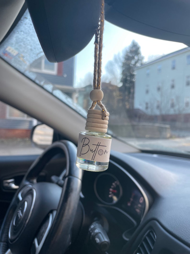 Pu&ograve; includere: Un profumatore per auto appeso allo specchietto retrovisore. Il profumatore &egrave; una piccola bottiglia di vetro con un tappo di legno e un'etichetta che dice "Button".