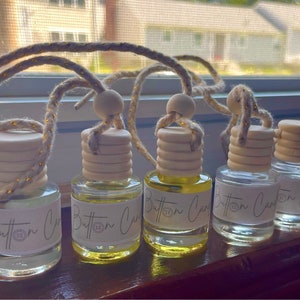 Pu&ograve; includere: Cinque bottiglie di vetro trasparente con tappi di legno e uno spago dorato che pende da esse. Ogni bottiglia ha un'etichetta bianca con la scritta "Button Car" stampata su di essa.