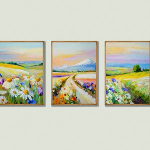 Op de afbeelding: Drie ingelijste landschapschilderijen met een landelijk tafereel van een kronkelende weg door een veld vol wilde bloemen. De schilderijen zijn in een licht houten lijst en hebben een zachte, impressionistische stijl.