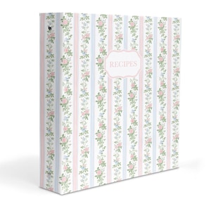 May include: A three-ring binder featuring a vertical striped pattern in light blue and pink, accented with floral vines of green leaves and small pink flowers. A central white label with a pink border displays the word RECIPES in pink text.