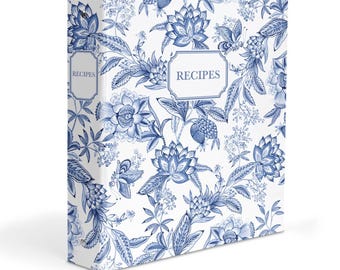 May include: A white three-ring binder featuring a blue floral pattern and the word RECIPES printed in a rectangular frame on the front cover and on the spine. The design consists of various blue botanical illustrations on a solid white background.