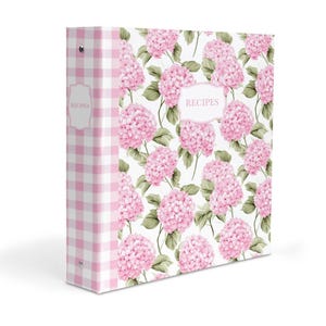 Puede incluir: Una carpeta de tres anillas con el lomo de cuadros vichy blancos y rosas y una portada decorada con un patrón de flores de hortensia rosas y hojas verdes. La palabra RECIPES está impresa en un marco de etiqueta blanco en el lomo y la portada.