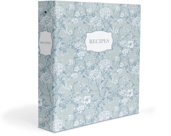 May include: A light blue three-ring binder featuring a white floral pattern and a central white label with the text RECIPES. The spine also includes a smaller white label with the text RECIPES. The binder has a metal ring mechanism.