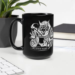 K&ouml;nnte beinhalten: Schwarze Keramiktasse mit einer wei&szlig;en Grafik eines Werwolfs, der eine Tasse Kaffee h&auml;lt. Das Design enth&auml;lt den Text "PLAYER NAME" am unteren Rand. Die Tasse steht auf einer wei&szlig;en Oberfl&auml;che.