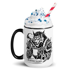 K&ouml;nnte beinhalten: Wei&szlig;e Keramik-Tasse mit schwarzem Henkel und Rand, mit einer Schwarz-Wei&szlig;-Illustration eines Werwolfs, der eine Tasse h&auml;lt. Die Tasse ist mit Schlagsahne, blauen Streuseln und einem rot-wei&szlig; gestreiften Strohhalm bedeckt. Der Text "PLAYER NAME" steht darunter.
