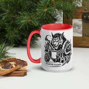 K&ouml;nnte beinhalten: Wei&szlig;e Keramiktasse mit roter Innenseite und Henkel. Die Tasse zeigt eine schwarz-wei&szlig;e Illustration eines Werwolfs, der eine Tasse h&auml;lt. Der Text "PLAYER NAME" ist auf der Unterseite der Tasse aufgedruckt.