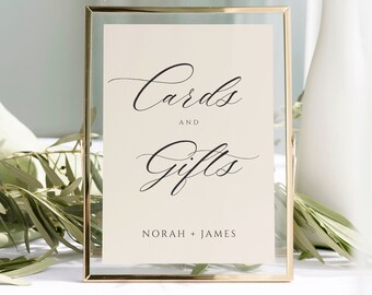 May include: A gold-framed sign with a white background and black calligraphy that reads "Cards and Gifts Norah + James".
