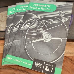 Könnte beinhalten: Ein Stapel von drei alten Ford-Servicehandbüchern mit grünem Einband. Das oberste Handbuch trägt den Titel "FORDOMATIC Service Review" und zeigt ein Schwarzweißfoto eines Armaturenbretts und Lenkrads eines Autos. Das unterste Handbuch trägt den Text "FORD SERVICE FORUM 1953 BOOKLET No. 7".
