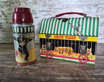 Fiambrera metálica vintage con forma de carro de circo y termo a juego. Diseño colorido de jaula de animales. Juego completo de fiambrera.
