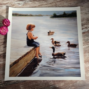 May include: A young girl in a blue dress sits on a wooden dock, watching ducks swimming in a lake. The ducks are brown and white with long necks and beaks. The lake is calm and blue, reflecting the sky and trees.