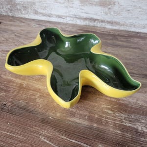 May include: A ceramic bowl with an irregular, organic star-like shape. The interior of the bowl features a glossy dark forest green glaze, while the exterior and the wide, undulating rim are finished in a bright, solid yellow glaze.