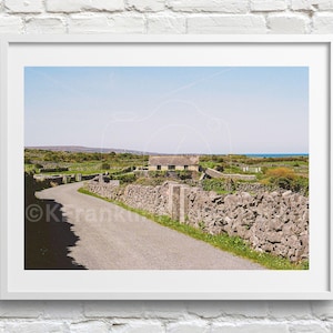 May include: Framed print depicting a rural scene with a winding road, stone walls, and a building with a thatched roof. The image is set under a clear blue sky, conveying a sense of peace and natural beauty.