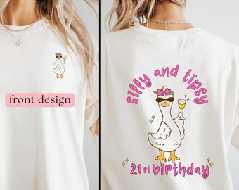 Puede incluir: Camiseta color crema con un pato de dibujos animados con gafas de sol y un cóctel. El diseño frontal muestra el pato, mientras que la parte trasera presenta las palabras "Silly and Tipsy" y "21st Birthday" en rosa.