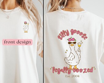 Puede incluir: Camiseta de color crema con un dibujo de un ganso de dibujos animados con gafas de sol y una copa de vino. El diseño frontal muestra el ganso, mientras que la parte trasera presenta las palabras "Silly Goose" y "Legally Boozed" con "Est. 2004".