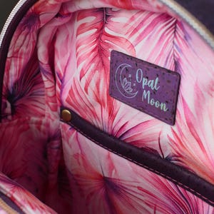 May include: Close-up of the interior of a purple backpack. The lining features a vibrant pink and red tropical leaf pattern. A purple rectangular patch with the text "Opal Moon" is visible.