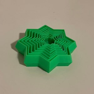 May include: A set of eight green star-shaped cookie cutters, nested inside each other, with the smallest cutter in the center.