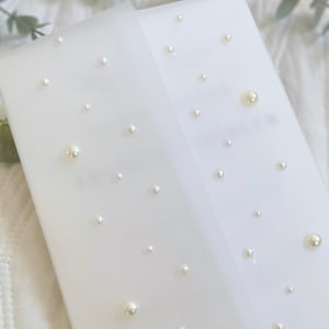 May include: A white envelope with a delicate pearl design. The envelope is made of a translucent material, and the pearls are scattered randomly across the surface.