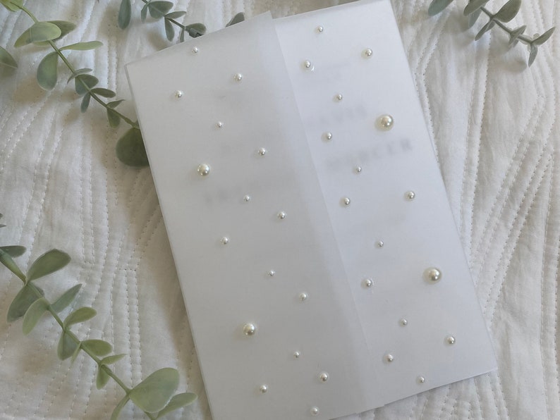 May include: A white card with a pearl design. The card is folded in half and has a white background with small, white pearls scattered across the surface.