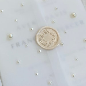 May include: A white envelope with a wax seal and pearl embellishments. The wax seal features a floral design.