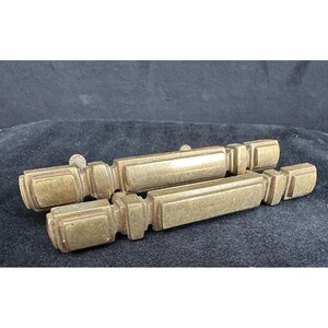 May include: Two antique brass drawer pulls with a rectangular design. The pulls have a warm, golden hue and are likely made of solid brass. Each pull has a decorative, geometric shape and a small, round knob on the end. These pulls are perfect for vintage furniture restoration.