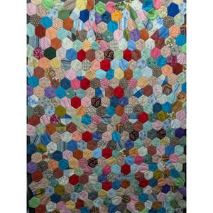 May include: A quilt constructed from numerous small fabric hexagons sewn together in a mosaic pattern. The textile features a wide variety of colors including red, blue, yellow, green, pink, and brown, with diverse patterns such as stripes, florals, and checks.