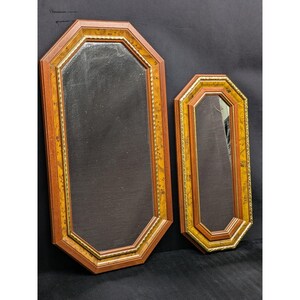 May include: Two octagonal mirrors with wooden frames. The frames feature a combination of dark and light brown wood, with a gold-colored trim. The mirrors have a dark, reflective surface.