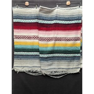 May include: Two woven blankets featuring horizontal stripes in shades of cream, light blue, dark blue, red, pink, yellow, and dark green. The blankets have a repeating geometric diamond pattern and frayed fringe edges at the bottom of each piece.