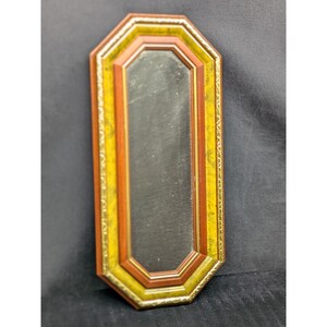 May include: An octagonal wall mirror with a long, rectangular reflective surface. The frame features layers of gold, yellow, and reddish-brown colors. The mirror is a decorative item.