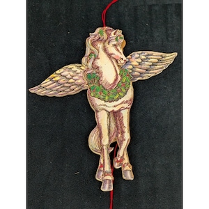 May include: A wooden Pegasus ornament with outstretched wings, a green and red holly wreath, and a red string for hanging. The Pegasus is cream-colored with detailed wings and a flowing mane. The ornament is likely for holiday or seasonal decor.