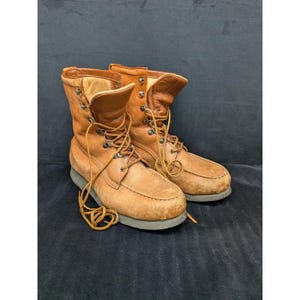 May include: A pair of tan leather boots with laces. The boots have a moccasin-style toe and a padded collar. The laces are tan and the soles are a dark gray. The boots appear to be well-worn.