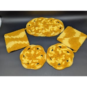May include: A collection of five handmade crochet items in shades of yellow and gold. The set includes two round trivets, two square potholders, and one oval-shaped trivet. The items feature a textured, woven design.
