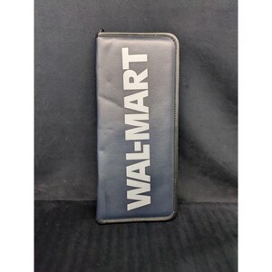 May include: A rectangular navy blue zippered case featuring the text WAL-MART printed in large, bold, light gray capital letters vertically along the front surface. The case has a smooth, matte finish and is outlined with a thin black border.
