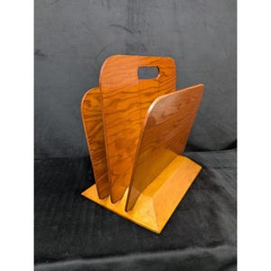 May include: A vintage wooden magazine rack with a handle. The rack has a light brown finish with visible wood grain. It features three vertical dividers and a rectangular base, perfect for organizing reading materials.