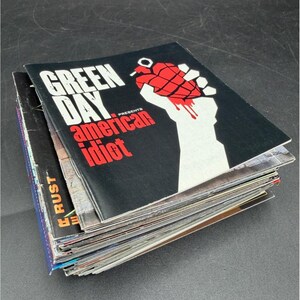 May include: A stack of magazines with the top one featuring the text "GREEN DAY PRESENTS AMERICAN IDIOT" in white and red on a black background. The cover art includes a red hand grenade in a white fist.
