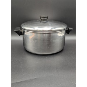 May include: Stainless steel cooking pot with lid. The pot has a brushed metal finish and black handles. The lid has a black knob. The pot is designed for cooking and food preparation.
