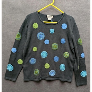 May include: A dark gray sweater with a crew neck and long sleeves. The sweater is decorated with various sized blue and green circles. The brand name "Timberlea" is visible on the tag.