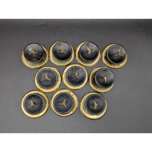 May include: A collection of ten vintage black and gold buttons. Each button features a black center with a gold emblem and a gold-toned outer ring. The buttons are arranged on a dark surface.