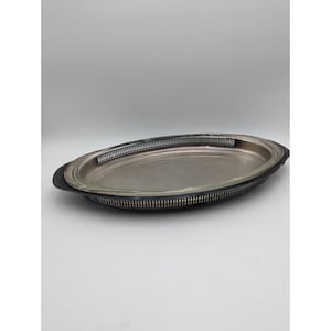 May include: Oval silver serving tray with a dark rim and a decorative pierced gallery. The tray has a shiny, reflective surface. A classic piece for serving food or displaying items.