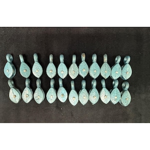 May include: A collection of twenty small, light blue metal pulleys arranged in two horizontal rows. Each pulley features a teardrop-shaped housing with a central rivet and a circular attachment loop at the top, displaying a textured finish.