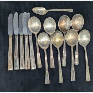 May include: A collection of silver-toned flatware including five knives with straight blades and eight spoons of varying sizes. Each piece features a decorative embossed pattern on the handle, showing signs of age and tarnishing on the metal surface.