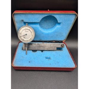 May include: A dial indicator gauge set in a red case with blue foam padding. The gauge has a white face with black markings and the brand name "Central". The set includes a metal measuring bar.