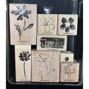 May include: A collection of seven wooden rubber stamps featuring various floral designs and the word Thanks. Each stamp block is made of light-colored wood and includes the text 2005 STAMPIN UP printed on the front surface of the wooden base.