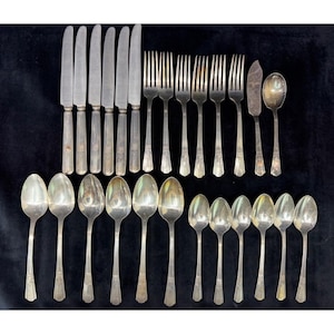 May include: A collection of silver-toned flatware consisting of six dinner knives, five dinner forks, one butter knife, one serving spoon, six large soup spoons, and six small teaspoons. Each piece features a simple, slender handle design.