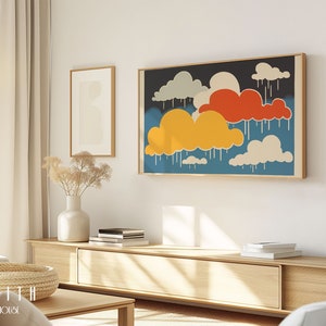 Op de afbeelding: Een ingelijste print van een kleurrijk abstract kunstwerk dat gestileerde wolken met regendruppels voorstelt. De wolken zijn in tinten rood, geel en wit tegen een blauwe achtergrond. De print hangt aan een witte muur boven een houten plank.