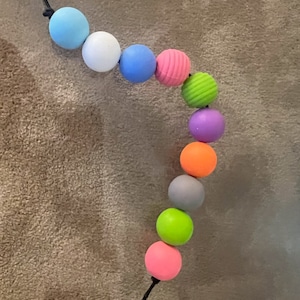 May include: A colorful string of beads with a variety of textures, including smooth, bumpy, and ribbed. The beads are in a rainbow of colors, including blue, white, light blue, pink, green, purple, orange, gray, lime green, and pink.
