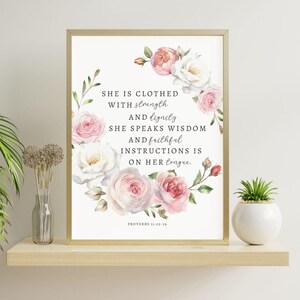 Könnte beinhalten: Ein druckbares Wandbild mit einem Blumenkranz aus rosa und weißen Rosen. Der Text lautet: "Sie ist bekleidet mit Stärke und Würde. Sie spricht Weisheit und treue Anweisungen sind auf ihrer Zunge. Sprichwörter 31:25-26"
