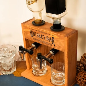 A wooden whiskey bar dispenser with two glass taps, one for whiskey and one for gin, along with a bottle of whiskey and a glass of ice.
