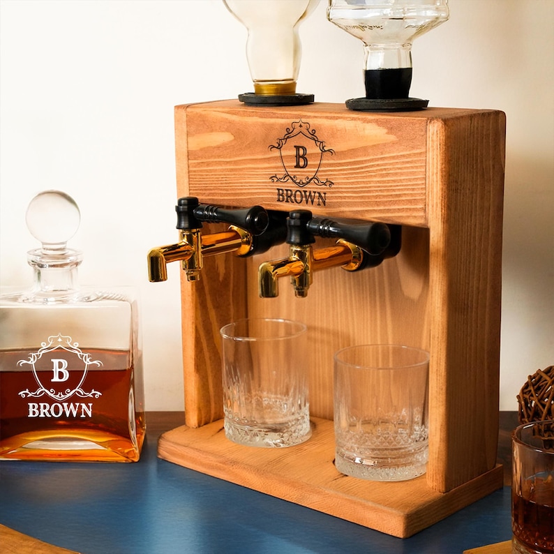 a wooden dispenser with two glass taps, a bottle of brown liquor, and two empty glasses on a wooden surface.