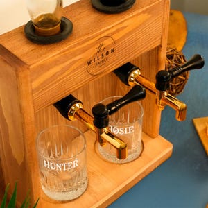 A wooden dispenser with two glass taps, each labeled with a different name.
